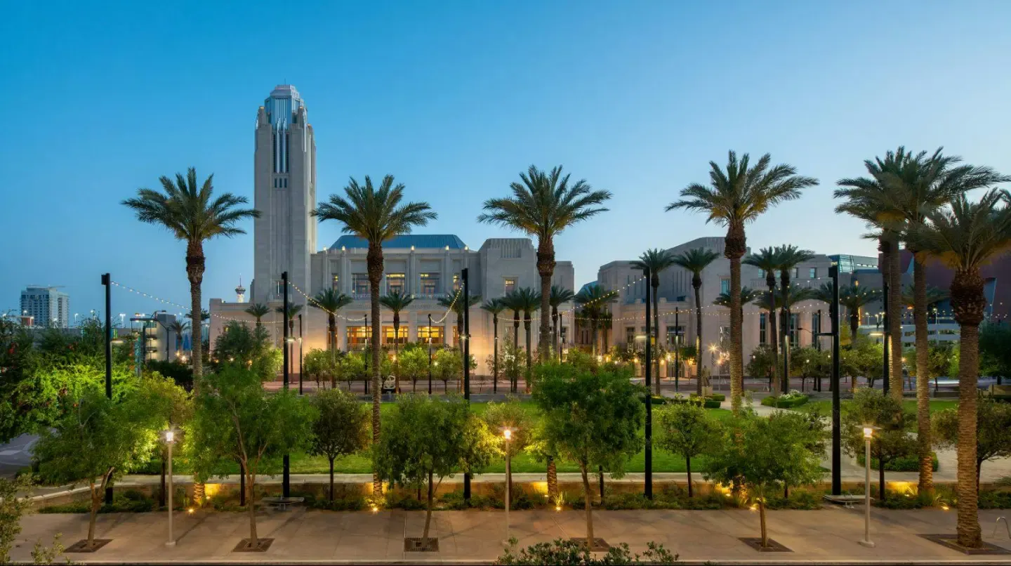 Palm-lined plaza at dusk with a tall downtown tower in the distance at Auric at Symphony Park