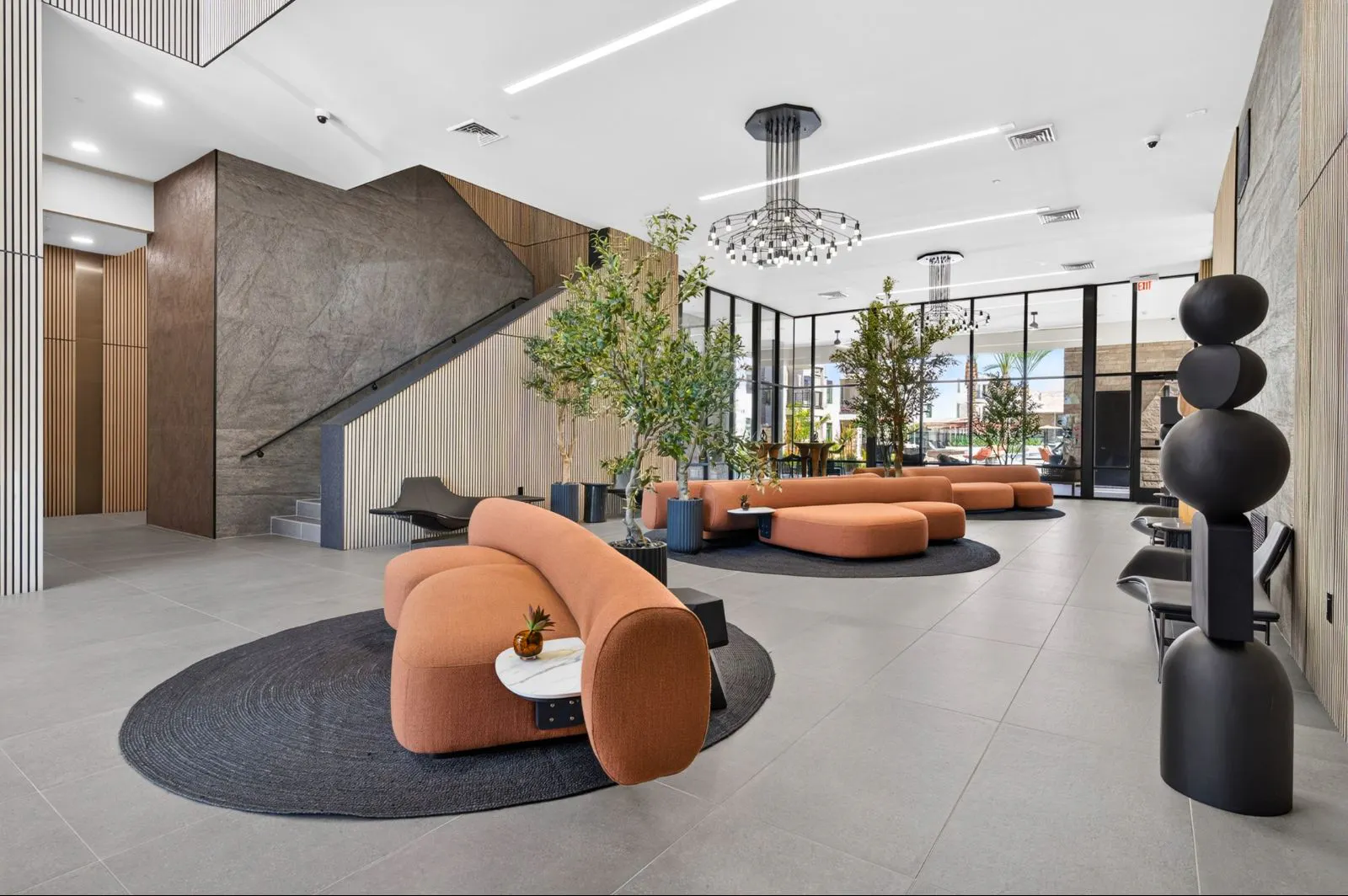 Lobby seating area with orange sofas and indoor trees at Harmony at Hawes Crossing