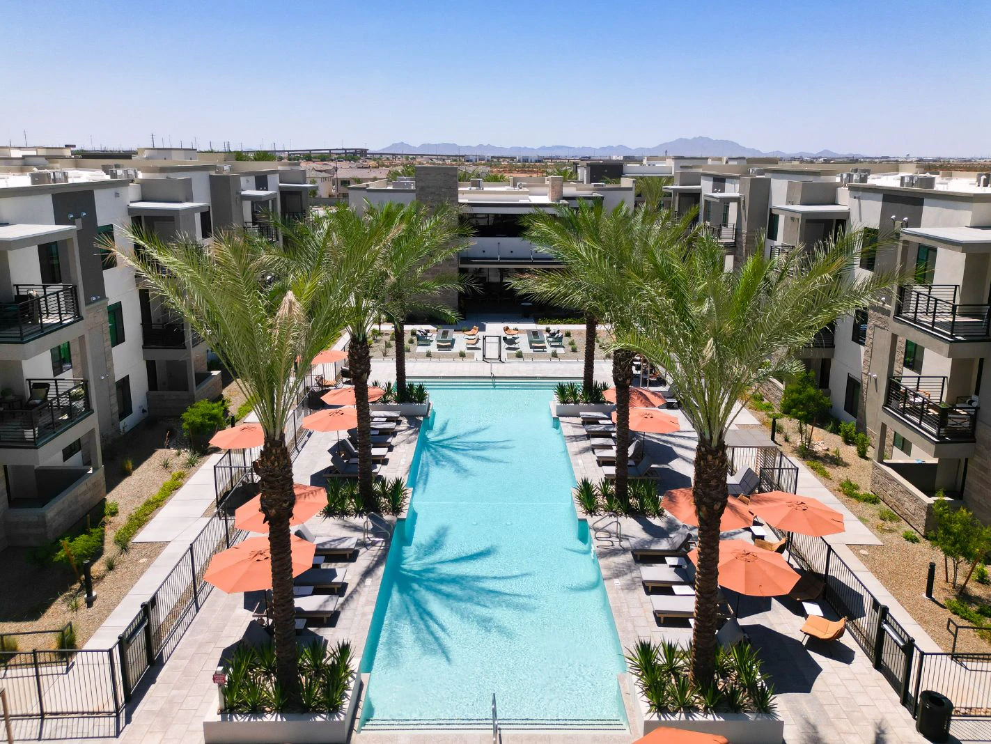 Long pool with palm trees and orange umbrellas between apartment buildings at Harmony at Hawes Crossing